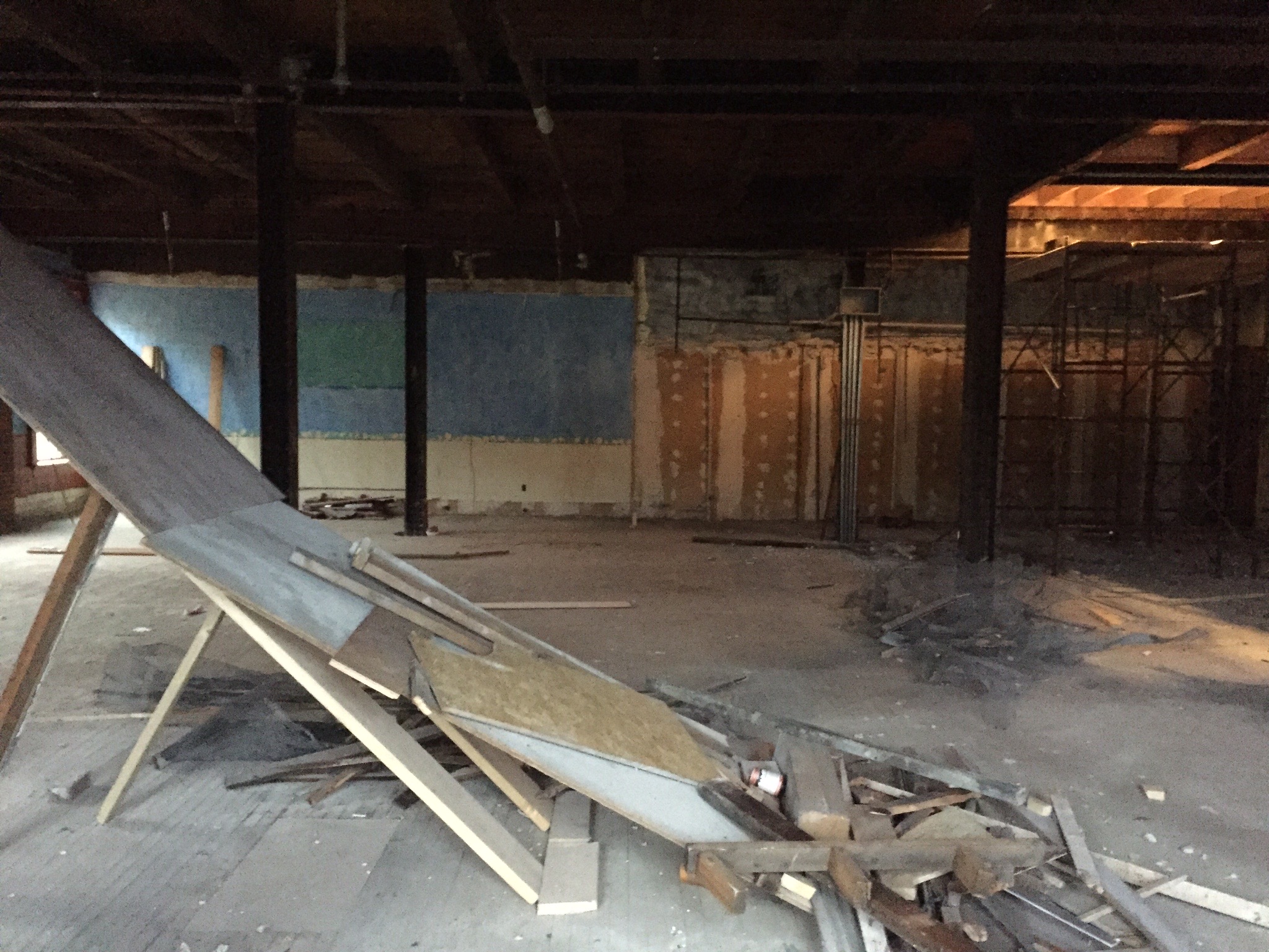 A gutted floor of a building, apprpoximately 60ft wide and just as deep, with some support I-beams throughout. There's a pile of wood scraps in the middle of the space that looks like a ramp, possibly for sliding debris down from a higher floor